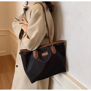 Detail of black nylon tote bag with brown leather handles worn by a model in a trench coat