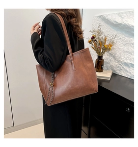 Close-up of brown leather tote bag with woven tassel detail worn by model at side