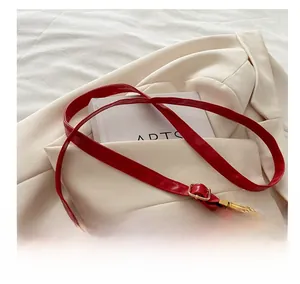 Detail of red patent leather shoulder strap with adjustable gold buckle for minimalist handbag