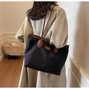 Large black tote bag with brown leather straps worn over a beige trench coat