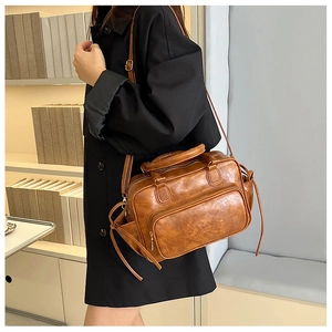 Brown vintage style leather handbag with top handle and adjustable shoulder strap worn by model
