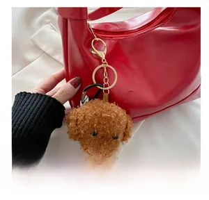 Detailed view of plush teddy bear charm with golden clip on a red handbag strap