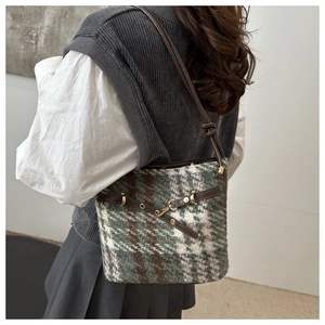 Mannequin portant un sac seau en tweed vert avec bandoulière et boucles dorées