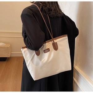 Detail of a beige canvas tote bag with brown leather handles worn by a model in a room