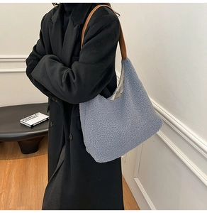 Detail of blue plush hobo bag with brown leather strap worn on a black wool coat