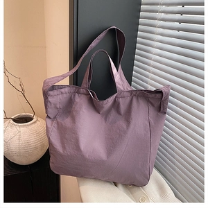 Dettaglio di una borsa tote in nylon viola con tracolla e manici su vestiti bianchi