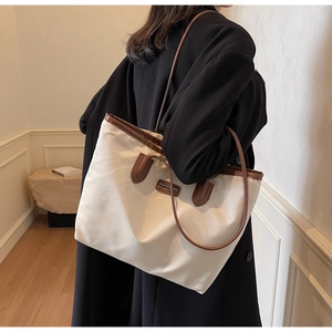 Detail of minimalist cream tote bag with brown leather straps worn on a black coat