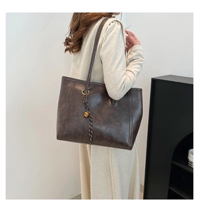 Detailed view of deep brown vintage tote bag with gold bell charm on a female model