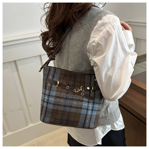 Détail d'un sac seau en laine à carreaux marron et bleu avec sangles en cuir et boucles dorées