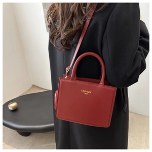 Detail of a dark red faux leather handbag featuring golden logo and top handle on black coat