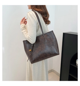 Detailed view of dark brown vintage tote bag featuring a decorative woven charm with gold ball