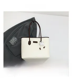 Detail view of large cream tote bag with brown handles and fuzzy monster charm accessory