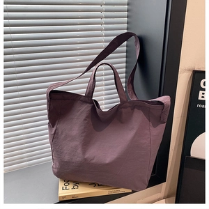 Dettaglio della grande borsa tote in tela viola scuro posta su un davanzale con dei libri