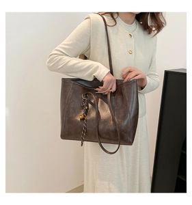 Detail of deep brown tote bag with leather texture and woven knot pendant decoration
