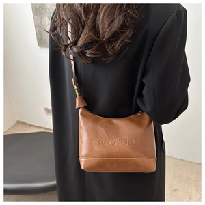 Detail view of caramel brown crossbody bag with minimalist embossed logo on matte leather