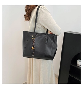 Detail of a chic black faux leather tote bag with long handles shown in use on shoulder