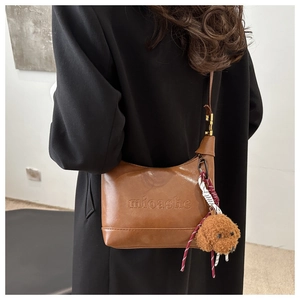 Close-up of brown leather hobo bag with teddy pendant worn over a black coat