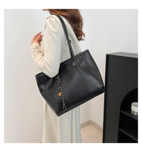 Detailed view of black tote bag featuring a leather texture and decorative bell charm