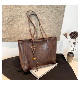 Detail of vintage brown leather tote bag with braided knot and gold bell charm