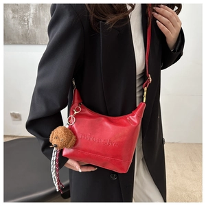 Detail of red leather shoulder bag with embossed texture and cute bear charm pendant