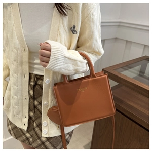 Brown leather tote bag featuring a round charm pouch and gold embossed fashion text