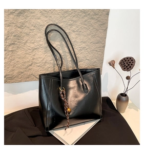 Detail of a black glossy tote bag with a woven rope charm and golden bell accessory