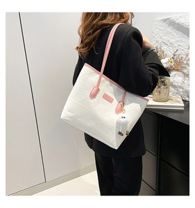 Detail of white textured tote bag with pink handles and a plush charm on a model