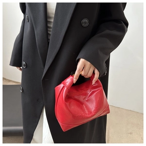 Detail of red micashe leather bag with pleated design over a black coat background