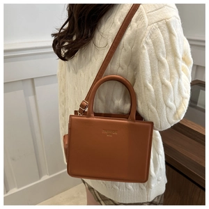 Rear view of brown PU leather shoulder bag worn over a beige sweater in cozy setting