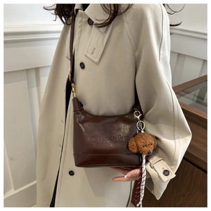 Detail of caramel leather shoulder bag with embossed logo and brown teddy bear charm