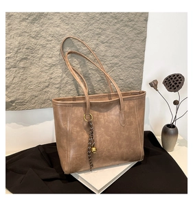 Detail of vintage brown tote bag with woven rope and metal bell pendant on white books