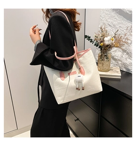 Detail of off-white tote bag with pink leather straps and a cute plush doll charm