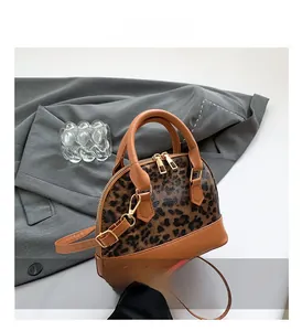 Detailed macro view of leopard print shell bag with brown leather handles and gold zippers