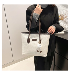 Detail of off-white embossed tote bag with brown straps and plush doll accessory