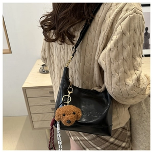 Detail of black leather shoulder bag with a cute teddy bear pendant and woven rope charm