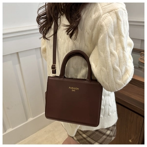 Detail of coffee brown leather handbag with gold Fashion Bag text and adjustable strap