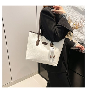 Detailed close-up of white embossed tote bag with brown handles and a plush charm