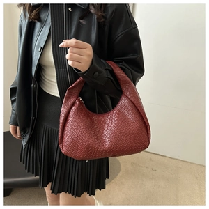 Deep red woven hobo bag with crescent shape held by model in casual street style