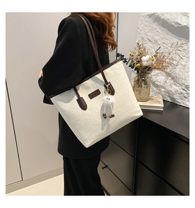 Detail view of large cream tote bag with letter embossing and plush pendant on model
