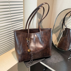 French vintage dark brown leather tote bag with elegant bell charm on wooden table