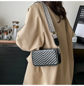 Détail d'un sac caméra noir matelassé en V avec une large bandoulière géométrique chic