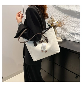 Detail of white tote bag featuring letter embossing and a white plush doll pendant