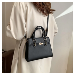 Detail of a black leather handbag featuring a golden turn-lock closure and slim strap