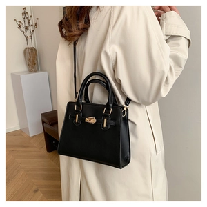 Detail view of black faux leather tote bag with gold hardware worn as a crossbody bag