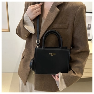 Detail of black PU leather shoulder bag with gold logo and round coin purse attachment