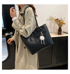 Close-up of black leather tote bag featuring embossed logo texture and cute plush charm