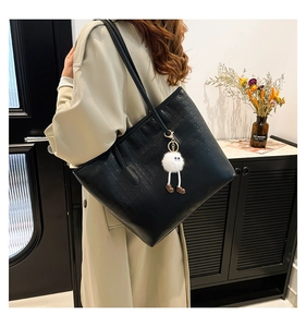 Detail of black tote bag featuring embossed patterns and a white plush toy charm