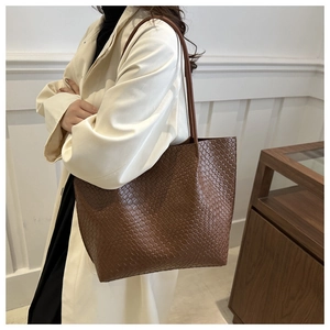 Brown woven leather tote bag shown on model wearing a trench coat for a commuter look