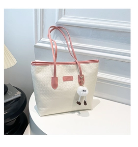 Detail of off-white leather tote bag with embossed texture and cute plush toy charm