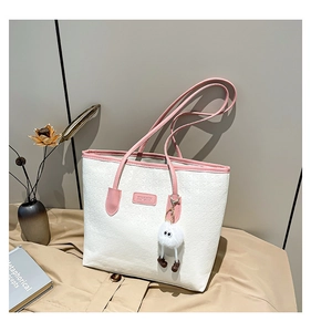 Detail of white quilted tote bag with pink trim and cute plush monster charm accessory
